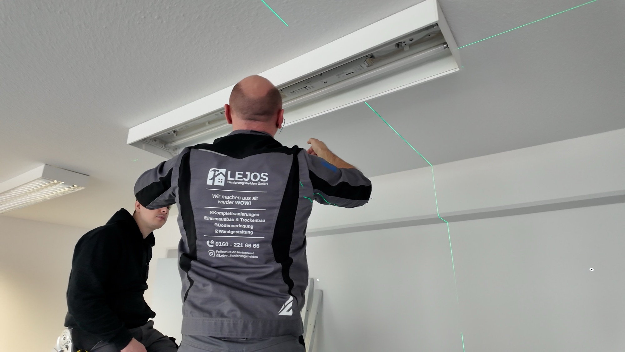 Zwei Monteure setzen eine Deckenleuchte nach eingemessener Laserlinie